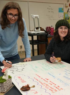 two students, a young man and woman, studying mushrooms with fun models in a biology class