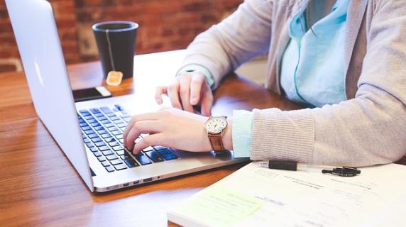 A BSN student in a cardigan studies nursing at a laptop with a textbook and a cup of tea