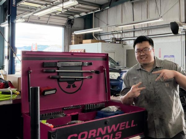 Leo Kim, an automotive and business student, wearing mechanics gear and smiling and posing in a garage 