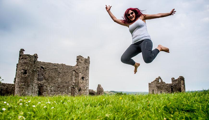 A student playfully jumps in a field in front of castle ruins