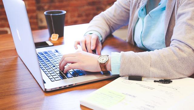 A BSN student in a cardigan studies nursing at a laptop with a textbook and a cup of tea