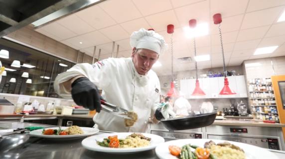 A culinary student in chef uniform plating food in the kitchen