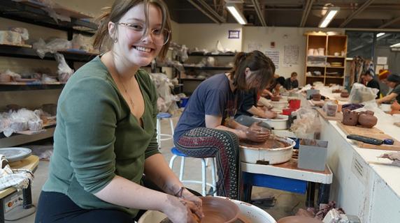 art student smiling and throwing clay at a wheel