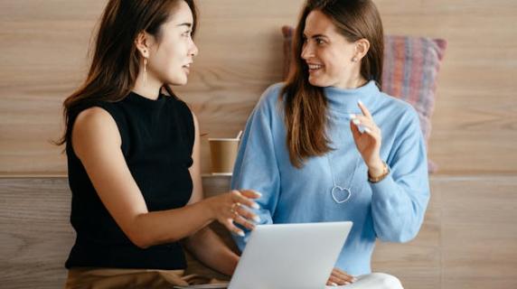 two women smiling and chatting with a laptop