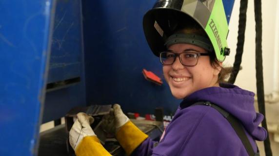 welding student with protective gear smiling at camera