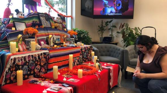 a young Latina woman sets up an ofreda with candle and marigolds in the Multicultural Center for Dia de los muertos