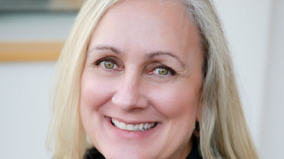 a woman with long blond hair, a black blouse, and stylish necklace