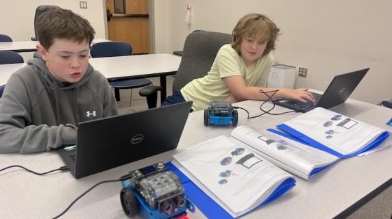 two middle schoolers program a small robot at computer summer camp