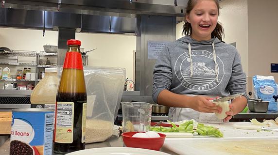 a high schooler laughs while she makes fried rice at culinary summer camp