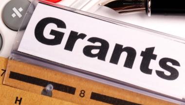 a calculator, pen, and file labeled "Grants"