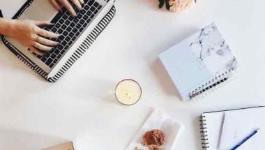 top view of someone working on a laptop with notebooks scattered
