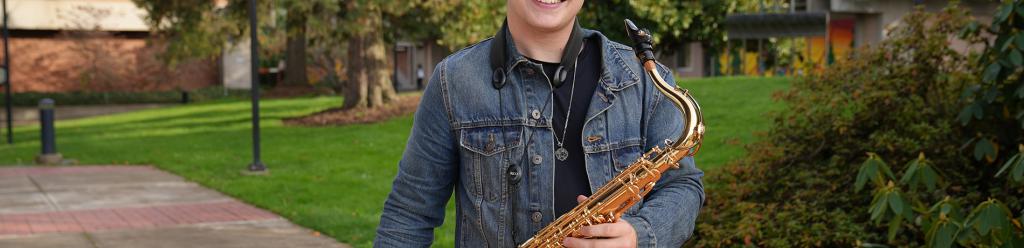 A music student in a jean jacket holding his saxophone and smiling