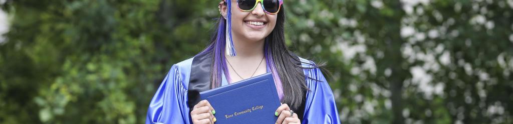 a graduating student in cap and gown with rainbow sunglasses