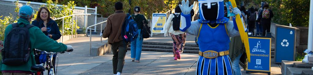 Ty the Titan mascot welcoming students at the entrance of campus with a welcome banner and fall foliage in the background