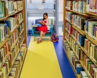 woman reading a book in between bookshelves