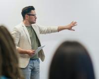 A man in a blazer and trendy glasses gives a business presentation