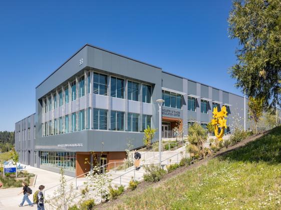 The exterior of the ITEC building on a sunny day with students and the bright yellow statue in front