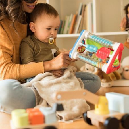 baby sitting in mother's lap surrounded by toys 